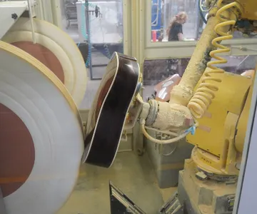 An industrial robot arm polishing a guitar body on a production line