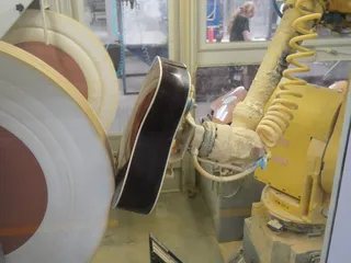 An industrial robot arm polishing a guitar body on a production line