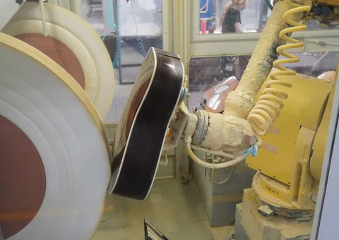 An industrial robot arm polishing a guitar body on a production line